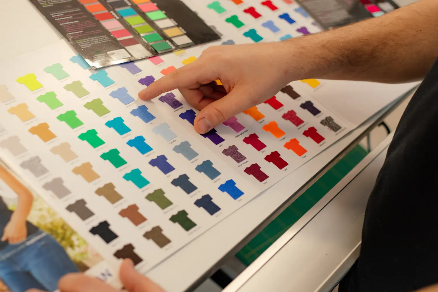 Zugeschnittene Männerhand, die Musterkatalog für mehrfarbige Werbe-T-Shirts mit Palette und Filmmembran auswählt. Textilproduktion